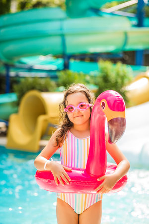 Happy kid little girl in an inflatable flamingo ring playing in outdoor swimming pool at sunny day. Active vacation and healthy lifestyle. Happy summertimeの写真素材