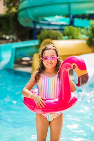 Happy kid little girl in an inflatable flamingo ring playing in outdoor swimming pool at sunny day. Active vacation and healthy lifestyle. Happy summertimeの写真素材