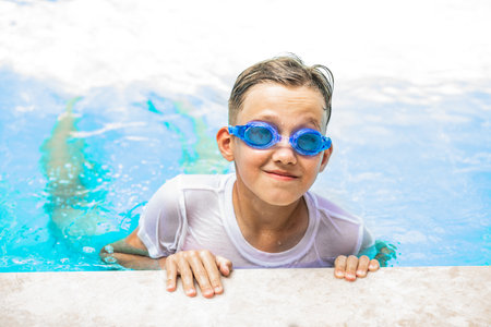 Happy kid boy playing in outdoor swimming pool at sunny day. Active vacation and healthy lifestyle. Happy summertimeの写真素材
