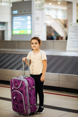 Adorable little girl in airport with suitcase waiting for boarding to flight. Active family lifestyle travel by air with child on vacation.の写真素材