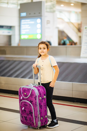Adorable little girl in airport with suitcase waiting for boarding to flight. Active family lifestyle travel by air with child on vacation.の写真素材