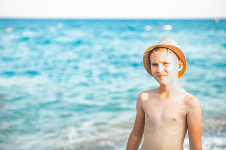 Cute kid boy teenager in a hat standing on the seashore nearby sea at the beach in summer. Playful active kid. Holiday vacation with childrenの写真素材
