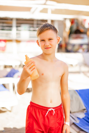 Cute little kid boy holding bottle of sunscreen in a hand at the beach in summer. Family holiday vacation with childrenの写真素材