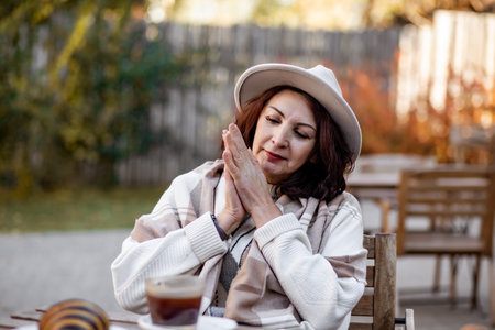 Middle aged woman sitting outdoor cafe and drinking coffeeの写真素材