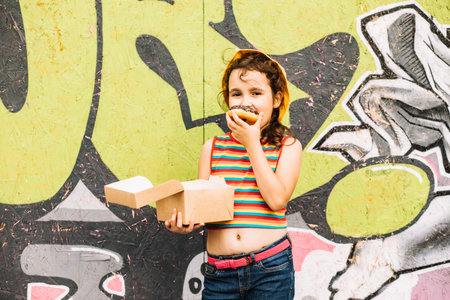 Little girl eating chocolate sweet and tasty donut. Child snacking on food outdoors.の写真素材