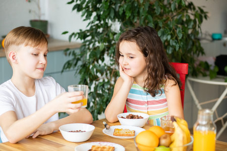 Happy family sister and brother have breakfast with cereal and milk in a kitchen at homeの写真素材
