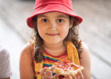 Cute little girl eating pizza. Children snacking on unhealthy food outdoors.の写真素材