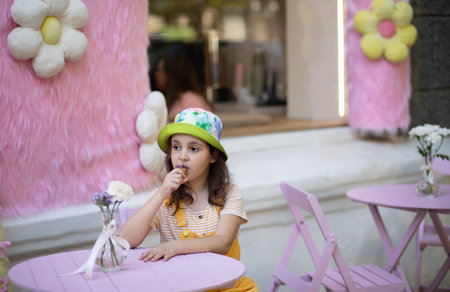 Cute little girl eating ice cream cone in hot summer outdoor cafe. Retro style.の写真素材