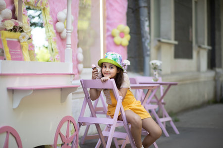 Cute little girl eating ice cream cone in hot summer outdoor cafe. Retro style.の写真素材