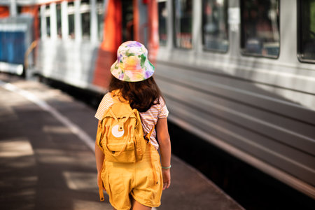 Cute little girl with backpack standing on the railway station platform waiting for a train. Travel,...