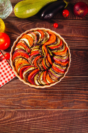 Homemade ratatouille with slices of zucchini, eggplant, tomato, red onion and herbs brushed with olive oil. Vegetarian meal.の写真素材