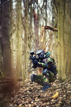 Paintball player in protective uniform and mask aiming gun in the forrest coverの写真素材