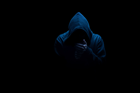 Man in black hood in the night darkness, dimly lit, concepts of danger crime terrorの写真素材