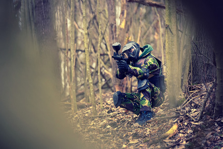 Paintball player in protective uniform and mask aiming gun in the forrest coverの写真素材