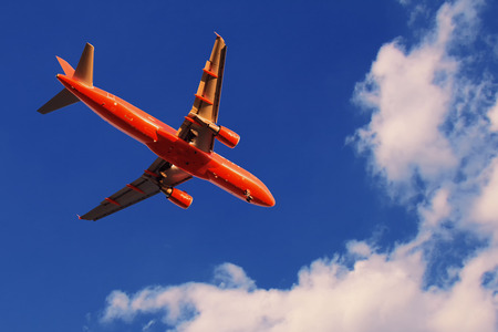 Red airplane in the sky at sunset with landing lights