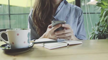 Woman using app on smartphone in cafe drinking coffee smiling and texting on mobile phone. Beautiful...