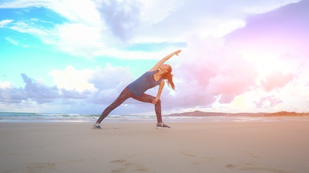 Woman is making yoga pose on beach in Vietnam. Sea or ocean happy female relaxation. Water and waves. Hands and blue sky. Exercises calmness and harmony. Sunny weatherの写真素材