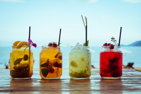 Set of iced cocktails: with lemongrass, berries, strawberry, peach, mint, lime decorated with flower, grass on sea beach backgroundの写真素材