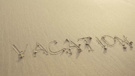 VACATION written on the beach sand washed aways by waves.の写真素材