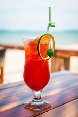 Close up of glass with refreshing orange cocktail with cherry on table on beach.の写真素材