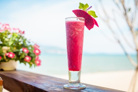 Close up of glass with refreshing orange cocktail with dragon fruit on beach.の写真素材