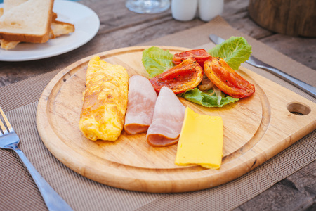Omelette with ham, greens, cheese and backed tomatoes served on cutting board.の写真素材