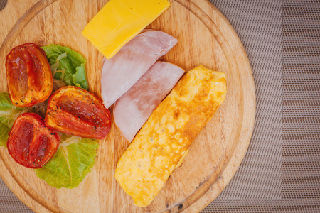 Omelette with ham, greens, cheese and backed tomatoes served on cutting board.