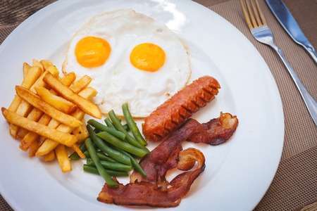 English breakfast with fried eggs, bacon, sausages, green beans and french friesの写真素材