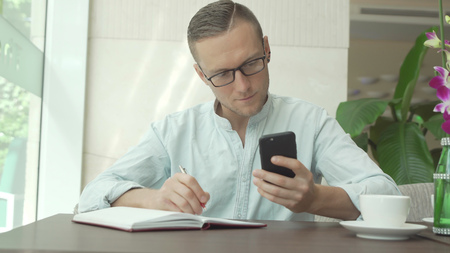 Businessman writing in daily planner and check notes on smartphoneの写真素材