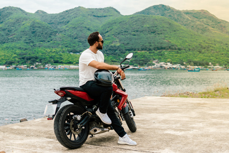Man sitting on his motorbike, holding helmet on sea backgroundの写真素材