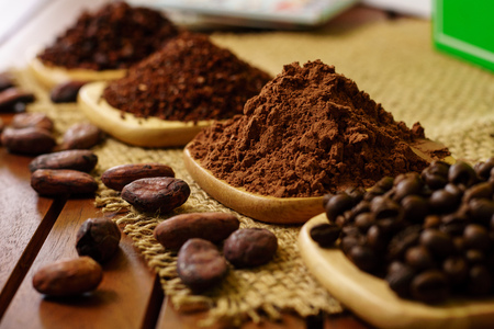 Cacao powder, cocoa nibs, and coffee beans on wooden plates on burlapの写真素材
