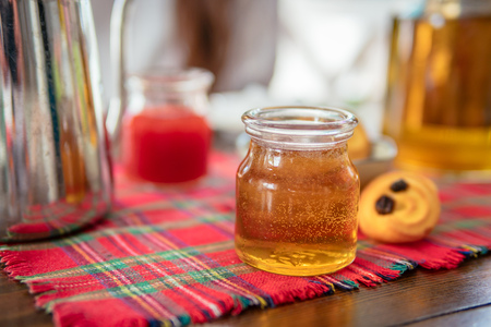 Jar of homemade honey on table. Strawberry jam and cookies on background.の写真素材