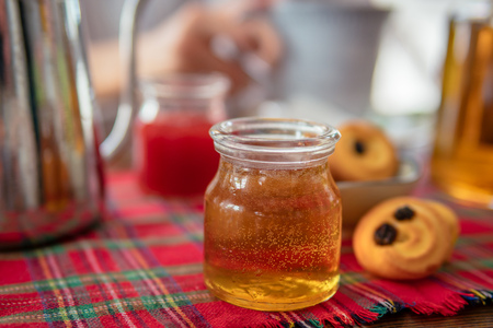 Jar of homemade honey on table. Strawberry jam and cookies on background.の写真素材