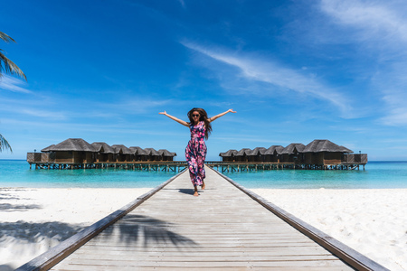 Happy woman with raised hands on bridge on beach in Maldivesの写真素材