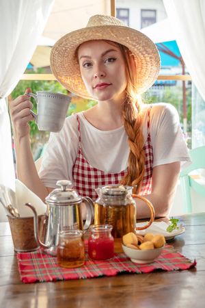 Country girl drinking tea. Tea pot, homemade honey, jam, muffins on tableの写真素材
