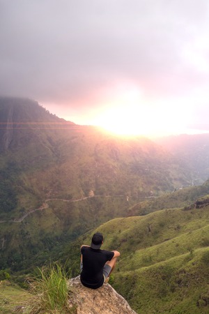 Man sitting on the top of Small Adams peak watching sunset. Ella, Sri Lankaの写真素材