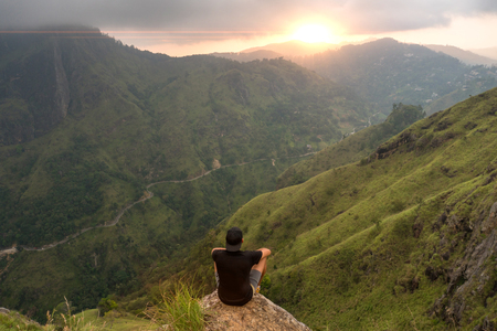 Man sitting on the top of Small Adams peak watching sunset. Ella, Sri Lankaの写真素材
