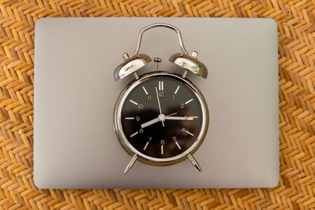 Alarm clock on laptop on braided texture. Online working concept.の写真素材