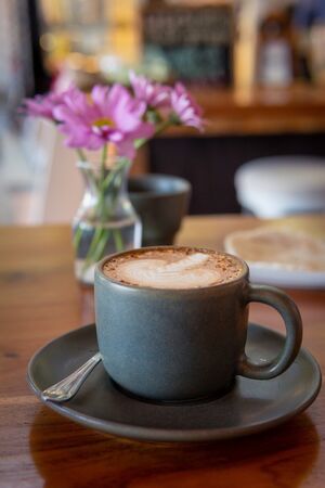 Cup of coffee and flowers on a wooden table. Hot cappuccino with foam close upの写真素材