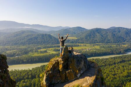 Young man standing victoriously on top of the mountain at sunrise. Aerial view.の写真素材