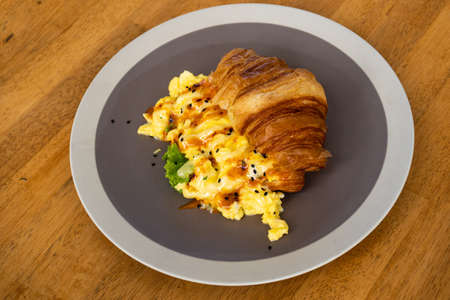 Hot breakfast croissant with egg on grey plate. Wooden table backgroundの写真素材