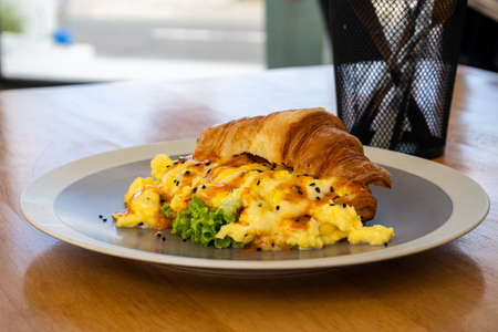 Hot breakfast croissant with egg on grey plate. Wooden table backgroundの写真素材