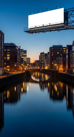 A large, blank billboard mockup for advertising hangs over a tranquil city canal at twilight, with illuminated buildings beautifully reflecting in the calm water.の素材
