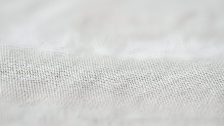A detailed macro photograph of a clean white fabric. Selective focus highlights the intricate woven texture, creating a soft, bright, and minimalist abstract background.の素材