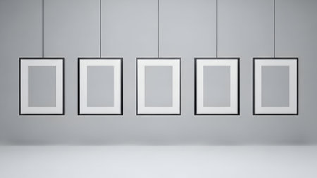 A clean, modern gallery showcases five identical empty picture frames, suspended by thin wires against a neutral gray wall.の素材
