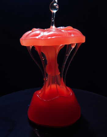 A drop of red paint falls into a vase on a black background.