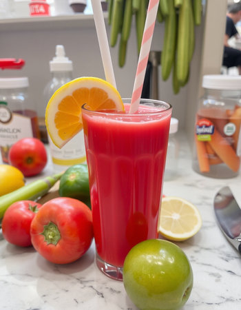 A glass of red smoothie with a straw surrounded by fresh fruits and vegetablesの写真素材