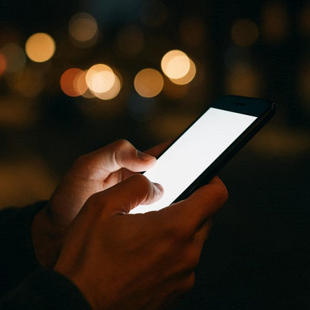 male hands holding a mobile phone with a blank screen in the night city