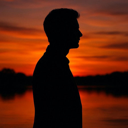 Silhouette of a man standing in front of a lake at sunset