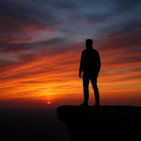 Silhouette of a man standing on top of a mountain at sunset